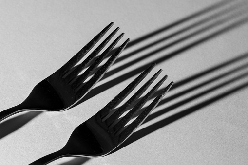 Two forks on a gray background with long shadows. Black and white. Creative minimal still life composition.