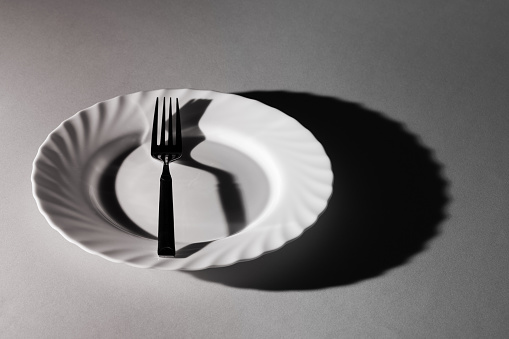 Un tenedor en un plato con sombras y texturas. Blanco y negro. Concepto surrealista creativo mínimo. Comer, utensilio para comer. Soledad del vacío. photo