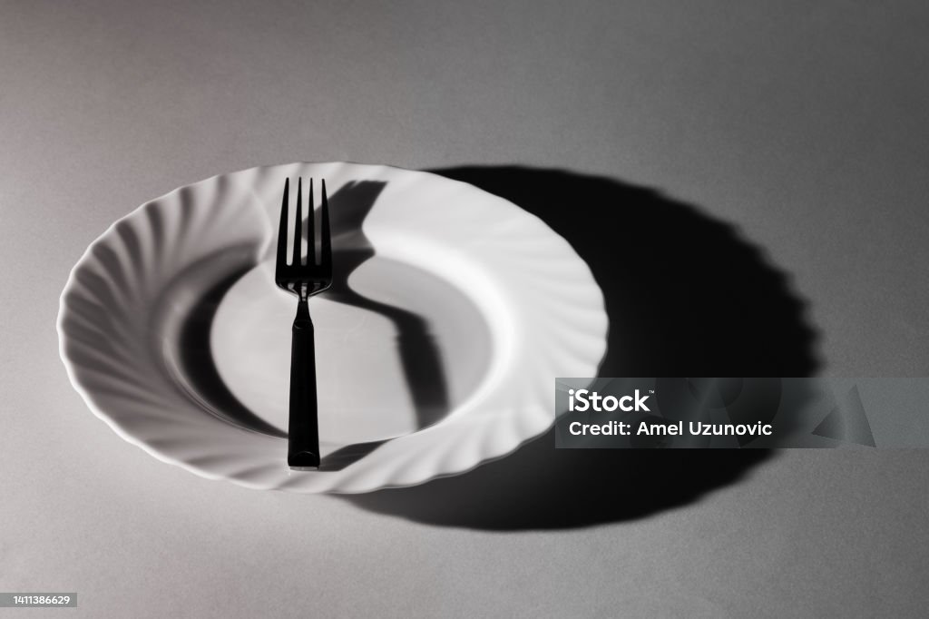 One fork in a plate with shadows and textures. Black and white. Minimal creative surreal concept. Eat, eating utensil. Emptiness loneliness. Hungry Stock Photo