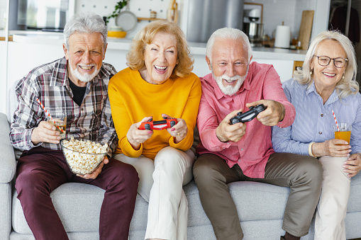 A small group of senior friends sitting on the sofa in the living room. They are playing video games