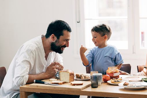 Caucasian father and his young son sitting at a table in their dining room, enjoying their meal together.
