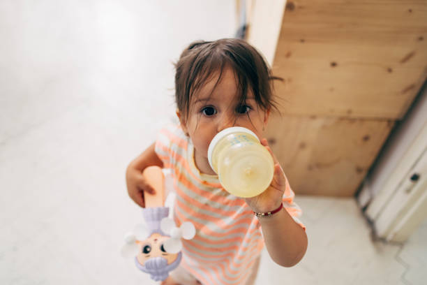 Portrait of a little baby girl drinking from a baby bottle, holding her toy and looking at the camera.