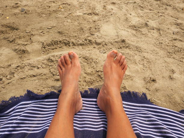 Beautiful photo of feet lying on a sandy beach with a blue and white towel.