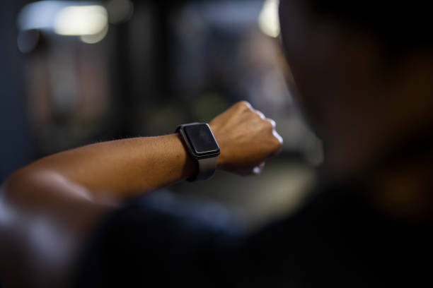Woman warming up riding exercise bike checking online trading on smart watch