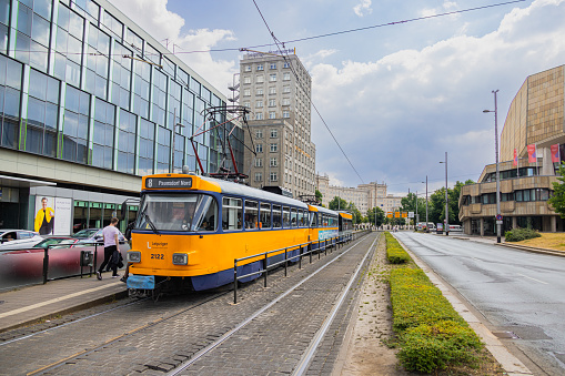 Leipzig, Germany - June 25, 2022: Leipzig tram at the Augustusplatz stop. Old tram in the city colors blue and yellow stops at a tram stop. People get on and off before the train moves on. City street