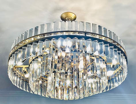Horizontal looking up to white ceiling that holds a large circular tiered clear crystal chandelier light fixture with gold trim