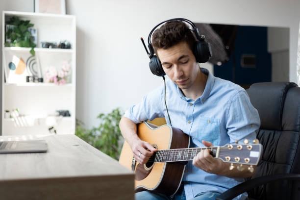 istock Young caucasian male practicing his guitar while wearing wired headphones 1411398163