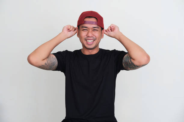 Tattooed asian man smiling excited while putting backward cap in his head