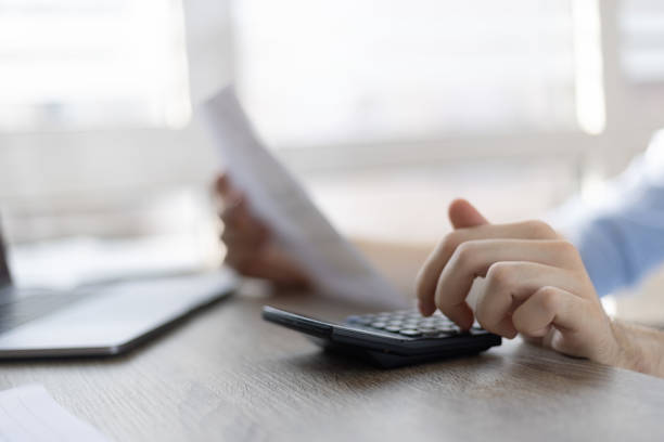 istock Close up businessman checking bills, holding receipt, using calculator, accountant calculating company expenses, financial report, sitting at wooden work desk, young male planning budget 1411399359