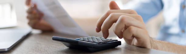 istock Close up businessman checking bills, holding receipt, using calculator, accountant calculating company expenses, financial report, sitting at wooden work desk, young male planning budget 1411399381