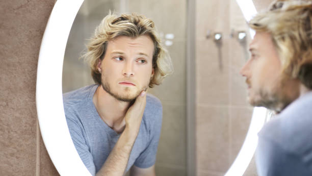 istock young man looking in the mirror,combing his hair,looking at problems on face 1411400947
