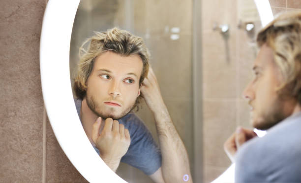 istock young man looking in the mirror,combing his hair,looking at problems on face 1411400950