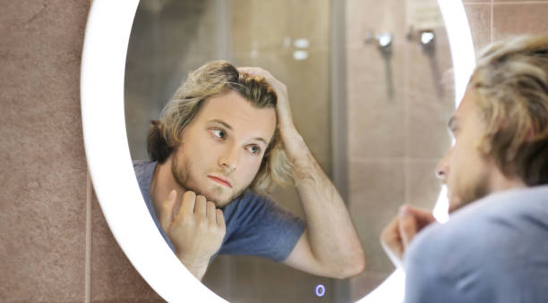 istock young man looking in the mirror,combing his hair,looking at problems on face 1411400954