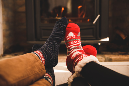 Couple warming their feet by the fireplace while wearing cozy Christmassy socks