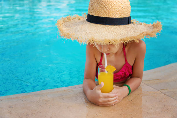 istock Girl In Straw Hat Drinking Orange Juice At Pool Side 1411402907