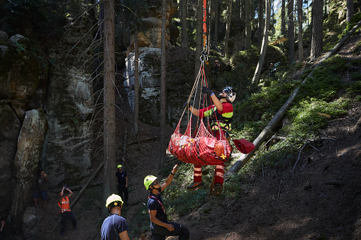 Adrspach, Czech Republic - July 24, 2022: Emergency medical doctor suspended from rope under helicopter during the rescue of injured tourist from difficult to access rocky terrain.