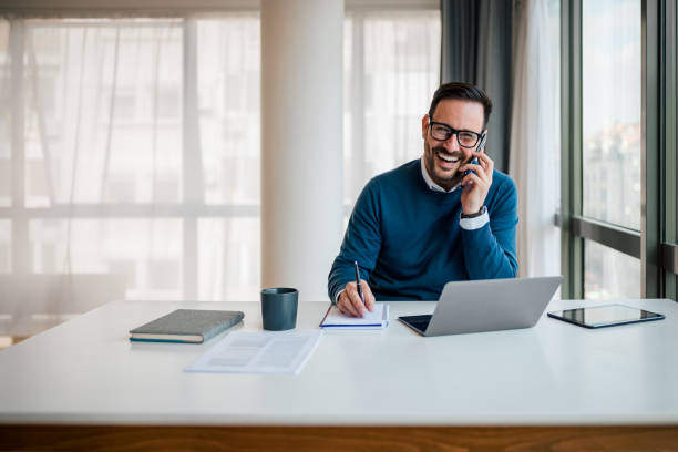istock Happy entrepreneur talking on smart phone while writing in diary at the office desk. 1411407543