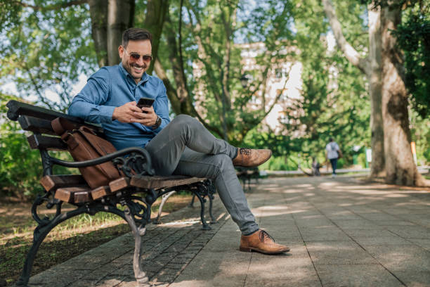 istock Smiling professional networking on smart phone while sitting on bench at the park. 1411407704