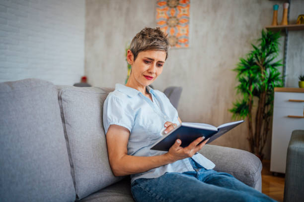 istock Woman reading a book on the sofa at home 1411409036