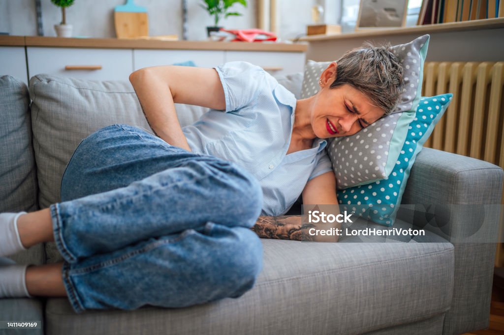 Woman suffering from stomach cramps Mature woman lying on her sofa alone and suffering from stomach cramps at home Endometriosis Stock Photo
