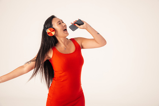 West Asian model going for portrait photos in studio. In this photo, she is standing and using phone and headphones for singing, looking away from camera.