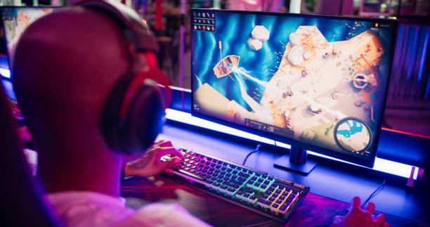 Pro gamer African ethnicity boy competing in video game eSport championship Pro esport male gamer playing competitive MOBA PvP top down view computer game on a stage. Wearing headset and talking into the microphone to communicate with pro team. Red and blue lighting. pc gaming monitor stock pictures, royalty-free photos & images