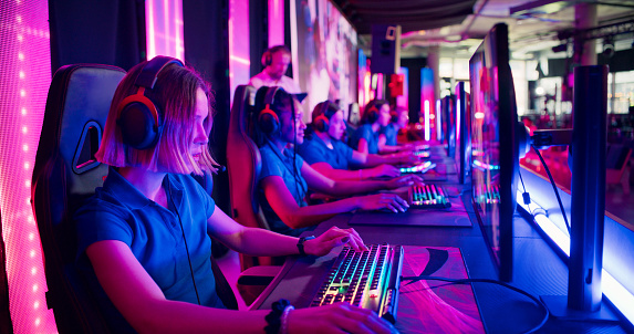 Diverse gamer group with african ethnicity female players playing competitive computer game in a gaming room. Wearing headset and talking into the microphone to communicate with the pro team and the coach.