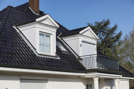 Daytime front view of the rooftop of a stone house with red tiled roof and cream colored painted vertical wooden planks in the top