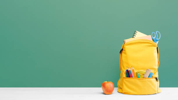 istock Backpack with different colorful stationery and apple on table and green background. Banner design back to school concept background. 1411417332