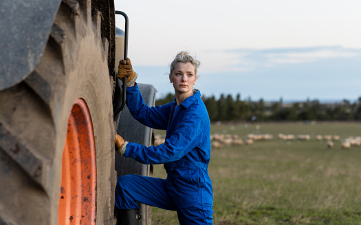 A selective focus of a female farming apprentice climbing up onto a tractor on a farm she is an apprentice on in Northumberland in the North East of England. She is using the tractor solo for the first time.
