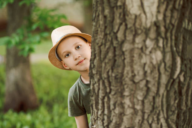 istock Little boy looking out from behind a tree. Summer activity. Happy childhood. 1411421672