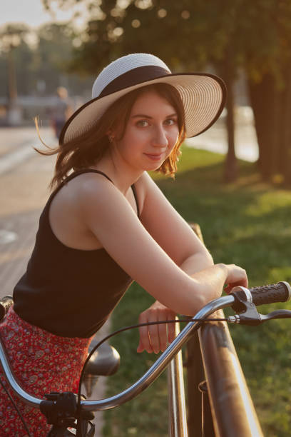 happy woman in hat posing with bike in sunny park