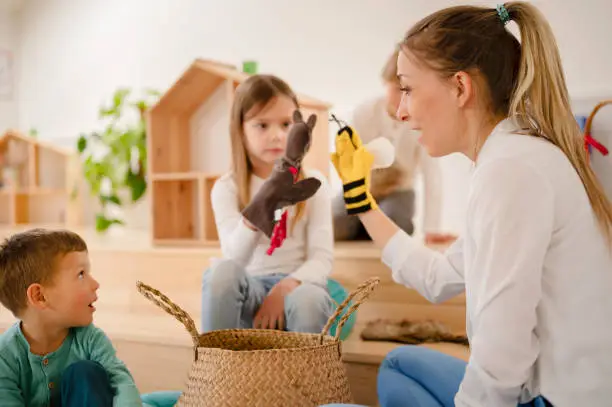 Photo of Teacher and preschool children playing with finger puppets