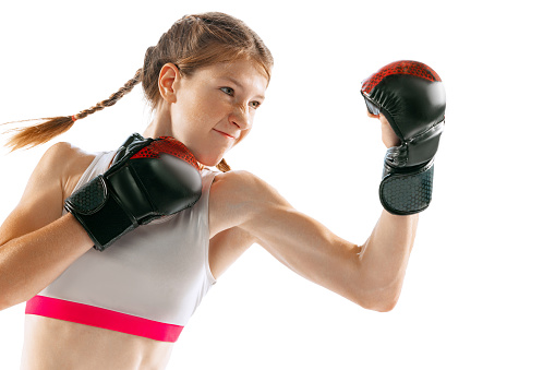 Punch. Portrait of sportive girl, junior MMA fighter in sports uniform and gloves training isolated on white background. Concept of sport, competition, action, health. Copy space for ad.