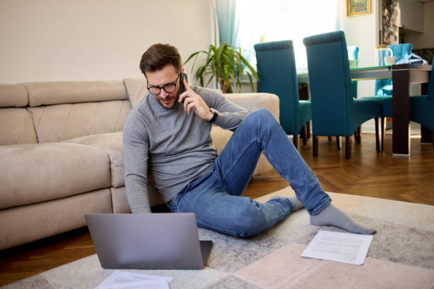 istock Mid adult man using his smart phone and laptop while working at home 1411425566