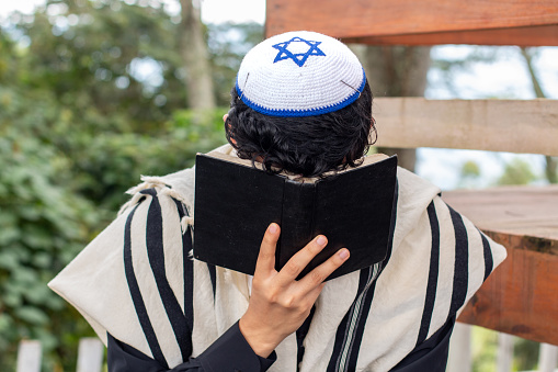 Frontal view of a Jew praying to his god and curving his face with a siddur.