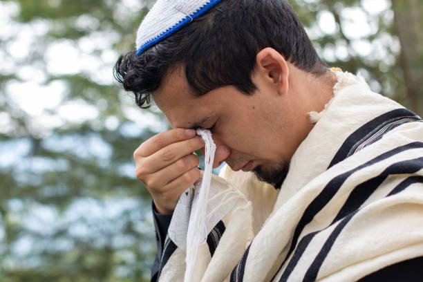 um judeu realiza um ritual de oração religiosa segurando o tzitzit aos olhos enquanto reza para seu deus. - talit - fotografias e filmes do acervo