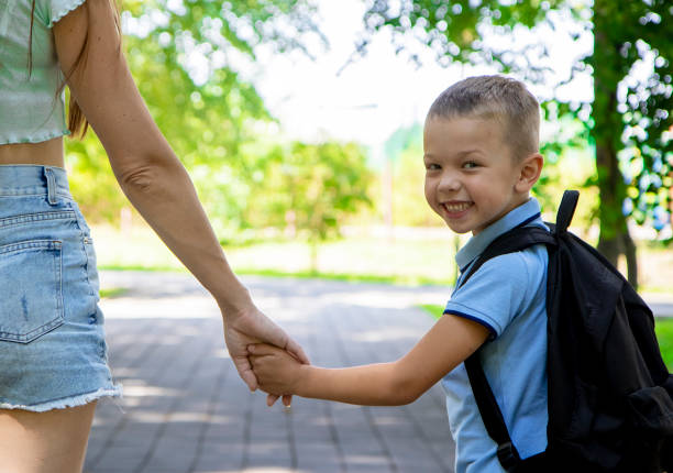 istock An elementary school student going to study. A first grader holds his mother's hand and smiles at the camera. The beginning of classes. A boy child with a backpack goes to primary school 1411427114