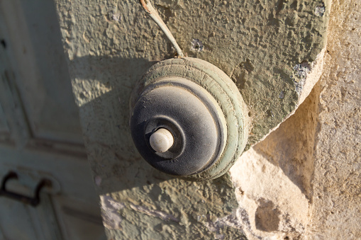 Closeup of a vintage doorbell on an old abandoned house with chipped stonework and peeling paint