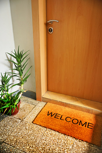 High angle view of a home front door with a welcome mat in front of it.