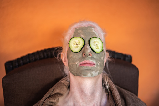 Woman in a spa with facial mask and cucumbers covering eyes