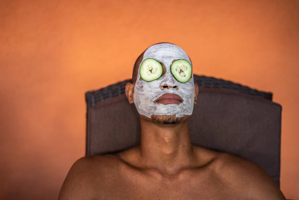 hombre en un spa con máscara facial y pepinos cubriendo los ojos - facial mask spa treatment cucumber human face fotografías e imágenes de stock