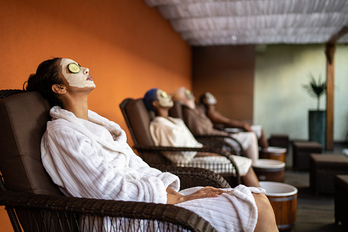 Group of people in a spa doing a foot treatment with facial mask and cucumbers covering eyes