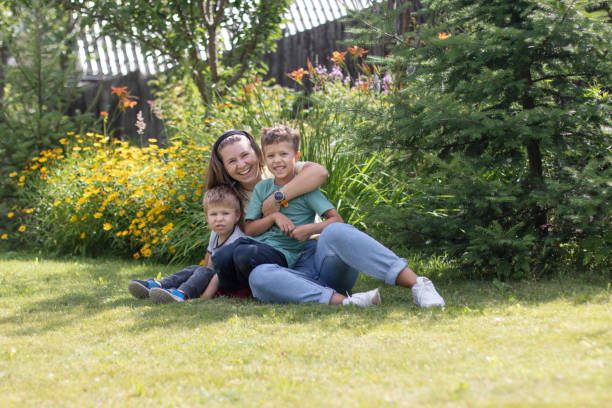 uma jovem está deitada na grama com seus dois filhos e eles estão rindo. conceito de maternidade feliz - embracing smiling gap children only - fotografias e filmes do acervo