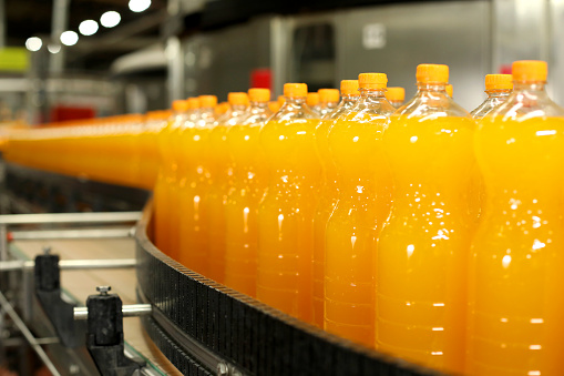 Production of carbonated drinks. Orange bottles on the production line
