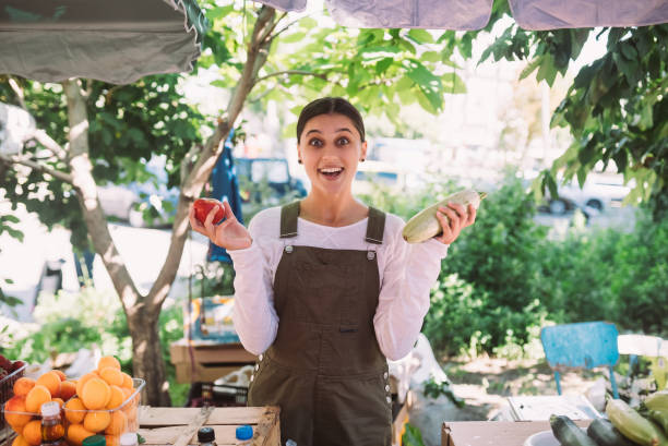 Young saleswoman holding zucchini and tomato in hands