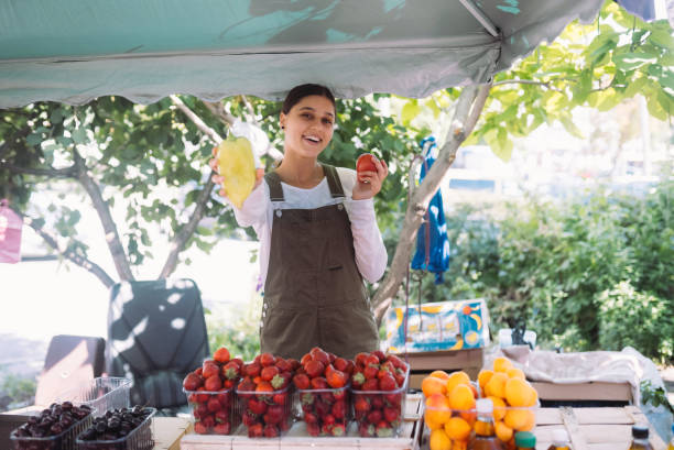 Young saleswoman holding bell pepper and tomato in hands