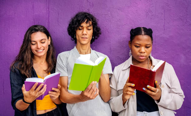 Three young friends reading books while leaning against a purple wall
