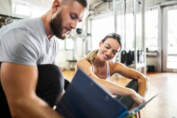 Coach planning sports training with his client Coach having sports training with young woman in a gym fitness instructor stock pictures, royalty-free photos & images