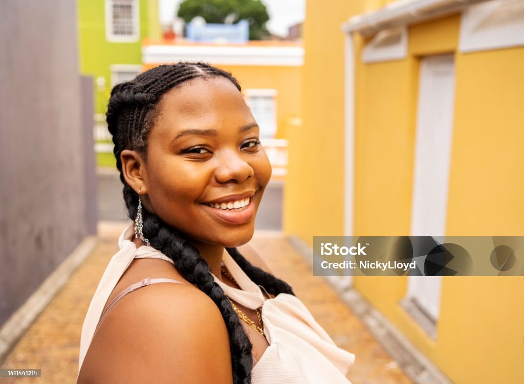 Smiling young woman walking down an alley with colorful buildings Portrait of a young African woman smiling while walking along a city alley surrounded by colorful buildings Street Stock Photo